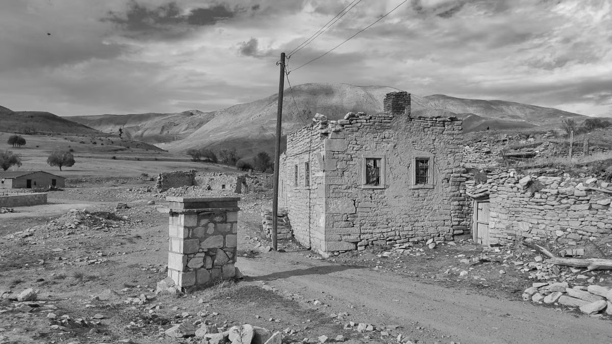 Black and white photo of an abandoned stone house in a barren desert landscape.